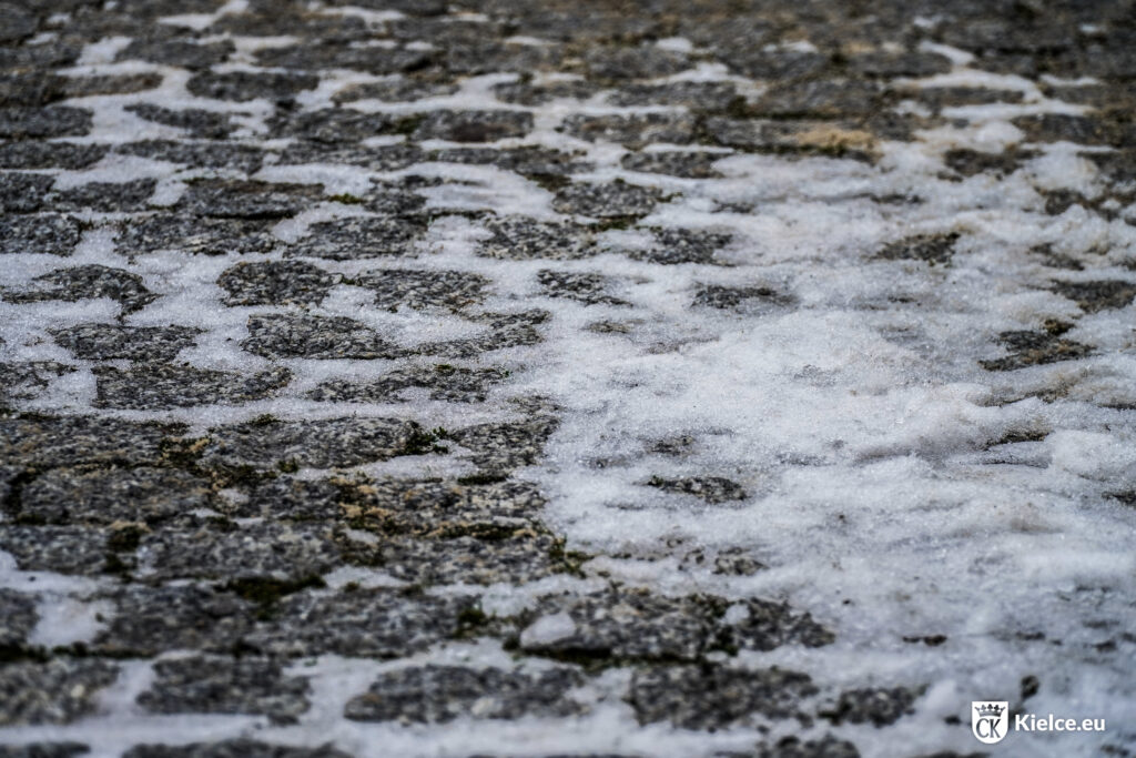 Fotografia prezentuje nawierzchnię ulicy z kostki granitowej pokrytą śniegiem i lodem.